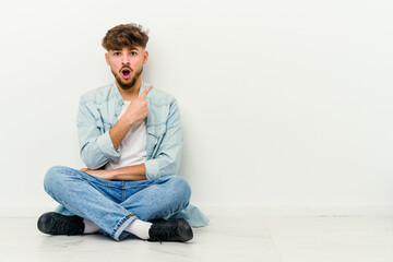 Young Moroccan man sitting on the floor isolated on white background pointing to the side