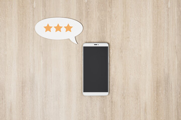Poster - Rating feedback review concept with blank black smartphone screen and speech bubble with three stars on wooden table. Mockup