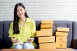 Young asian woman is entrepreneur looking phone and writing order of customer with online on notebook at home, online shopping, logistic and delivery, female is seller working on sofa, business SME.