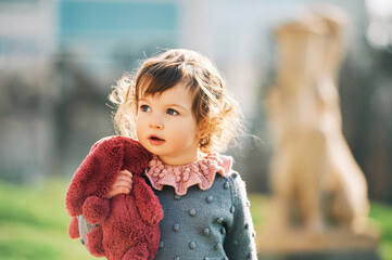 Outdoor portrait of adorable toddler girl playing wirh pink bunny toy