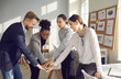 © Studio Romantic - Team of happy enthusiastic diverse business people and company employees smiling and joining hands in group office meeting as symbol of cooperation, teamwork, unity, corporate success and leadership