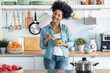 Beautiful afro woman eating noodles with chopsticks while looking at camera standing in the kitchen at home.