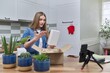 © Valerii Honcharuk - Woman recording video on smartphone unpacking cardboard box. Pet parrot helping to unpack