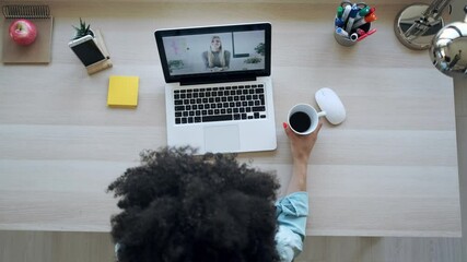 Wall Mural - Video of beautiful young afro business woman making video call with laptop while drinking coffee sitting in the office at home.