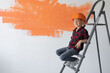 © Andrii Lysenko - boy dressed in protective orange sits on a construction ladder.