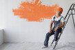 © Andrii Lysenko - a man in overalls is sitting on a ladder. Protective orange helmet on the head.