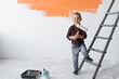 © Andrii Lysenko - A young boy with a smile stands in a room near the stairs. Holds a paint brush in his hands.