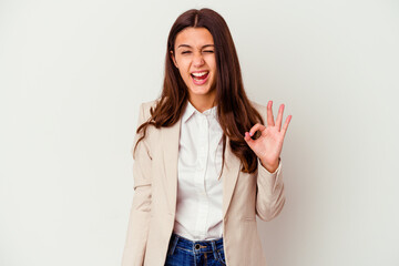 Young Indian business woman isolated on white background winks an eye and holds an okay gesture with hand.