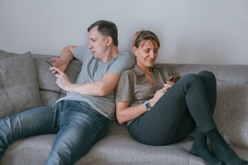 Man and woman sitting on a couch and holding smartphones in their hands.