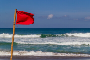 Red warning flag flapping in the wind on beach at stormy weather.