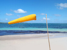 Yellow Windsock, Wind Sleeve Flying On A Blue Sky On French West Indies Beach With Turquoise Waters Of The Caribbean Sea. Idyllic Tropical Landscape. Wind Force And Direction Meter. Meteorology Tool.