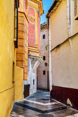 Old medieval narrow street with Spanish style colorful facades of buildings and blue sky in the background.