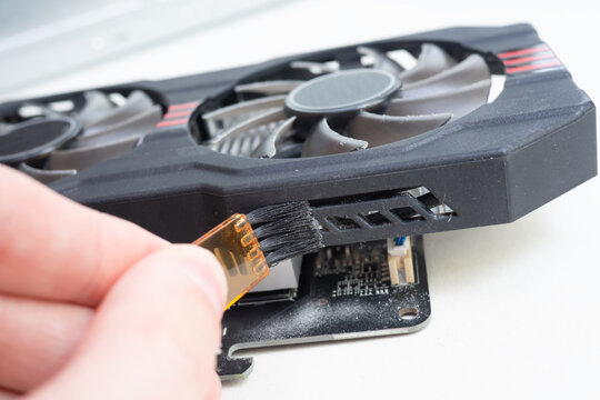 Close up of repairman cleaning dusty graphics card with brush on white table