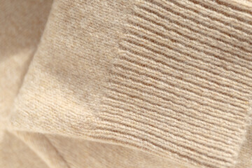 Details of a knitted wool sweater, textured background. A folded cashmere knit sweater in a beige shade. Stylish knitwear