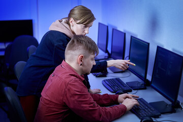 A man communicates with a colleague and discusses the work of a programmer. The woman points at the monitor of her personal computer. Esports player. Computer room. Work in the office.