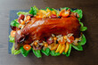 Restaurant menu. Baked suckling pig whole on a stone decorative board with fruit and physalis. Top view.