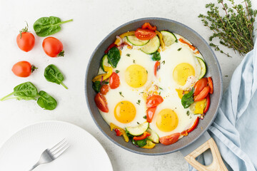 fried eggs poached with vegetables on teflon pan - pepper, tomatoes, spinach, peppers, onion and gar