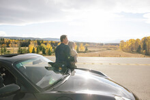 Couple Leaning On Sports Car In Front Of Forest