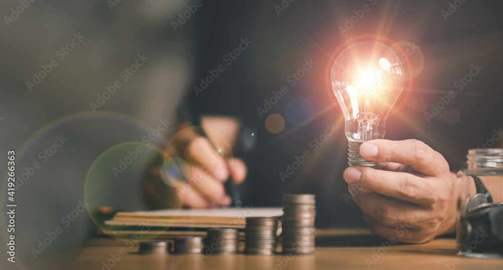 businessman holding lightbulb with using calculator to calculate and money stack. idea saving energy and accounting finance in home office concept, Business, finance, investment, Financial planning. - obrazy, fototapety, plakaty 