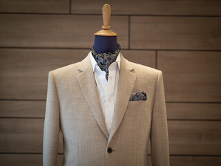 Wall Mural - Close up of beige jacket suit with white shirt and ascot tie scarf on mannequin. selective focus