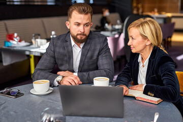 Wall Mural - two business colleagues discussing project using laptop, theysit in restaurant talking, co-working