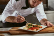 © Roman - Cook man neatly decorates the dish. young professional chef adding some piquancy to meal. in modern kitchen, at work in uniform