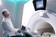 © Roman - Senior Radiologist Controls MRI or CT or PET Scan with Male Patient Undergoing Procedure. High-Tech Modern Medical Equipment. Friendly Doctor Working With Patient