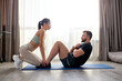 © Roman - female helps man to do abs exercises, supporting, fitness couple together at home, engaged in sport and wellbeing, want to be in good shape, during quarantine