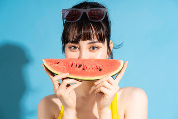 Wall Mural - Beautiful Asian woman wearing yellow jumpsuit on blue background and eating tropical fruits, summer concept