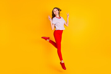 Wall Mural - Photo of charming funny lady jump show two v-signs wear striped shirt red pants shoes isolated yellow color background