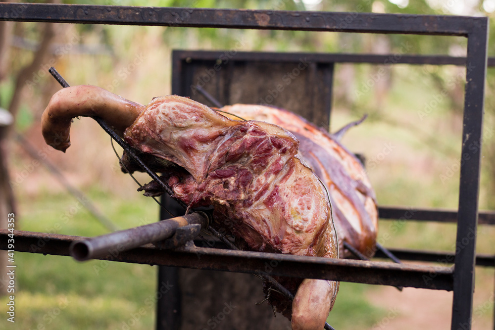 Pork roasted on a rotating spit on the grill. Front view with the ...