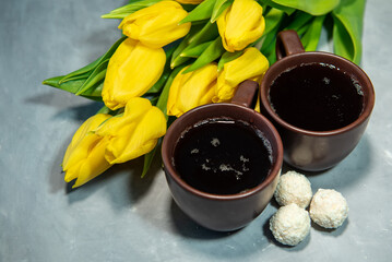 Wall Mural - Two cups of tea or coffee with sweets in coconut flakes. Tea, yellow tulips on a gray background. Close-up