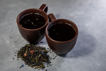 Two cups with tea and dried tea leaves on a gray background. Close-up. Place for text