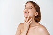 © Cookie Studio - Skin care beauty. Beautiful natural woman touching neck and smiling, looking aside. Girl laughing and showing glowing, hydrated facial skin, standing on white background