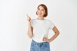 © Cookie Studio - Portrait of beautiful girl in t-shirt pointing finger left, smiling joyful at camera, showing way to logo, standing on white background