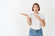 © Cookie Studio - Amazed female model holding item on palm, pointing at hand empty space as if showing product, advertising on white background