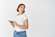 © Cookie Studio - Happy woman smiling and looking aside at empty space, using smartphone. Girl with mobile phone gazing at logo, standing against white background