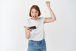 © Cookie Studio - Happy girl winning video game, raising hand and looking at smartphone excited, celebrating victory on mobile app, white background
