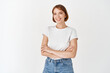 © Cookie Studio - Portrait of beautiful natural female model with short hair, wearing t-shirt with jeans, cross arms on chest and smile at camera with happy emotion, white background