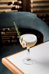 Wall Mural - Yellow cocktail with white foam and thyme in margarita glass on the table at restaurant