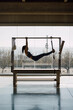 © BASILICOSTUDIO STOCK - Fit female instructor hanging hands and feet from the pilates machine, woman working out on the Trapeze Table in a big Fitness Studio with big windows and street views. Indoors, daytime.