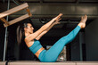 © BASILICOSTUDIO STOCK - Professional Pilates female coach practicing Pilates in a bench reformer machine, balancing exercise, in a big loft studio, with natural sun light on her, indoors, during daytime. Healthy lifestyle.