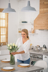 Wall Mural - Blonde housewife in jeans putting flowers into the vase