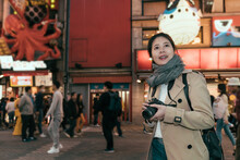 Sushi Restaurant With Fugu Pufferfish Balloon Statue And Takoyaki Octopus Sign In Background. Young Girl Cheerful Holding Camera Looking Up While Standing In Dotonbori Shopping Street Namba At Night.