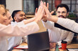 © Roman - Cheerful business team giving each other high five to success while working in the modern office