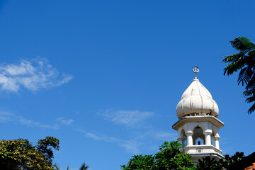 The dome of the mosque is white in color in isolation from the background of blue sky and white clouds