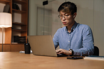 Sticker - Focused asian guy working with laptop while sitting at table in office