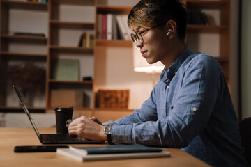 Sticker - Focused asian guy working with laptop while sitting at table in office