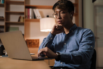 Sticker - Focused asian guy working with laptop while sitting at table in office