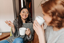 Selective Focus Of Good-humoured Friends Drinking Tea At Home. Two Charming Girls Talking And Enjoying Coffee.